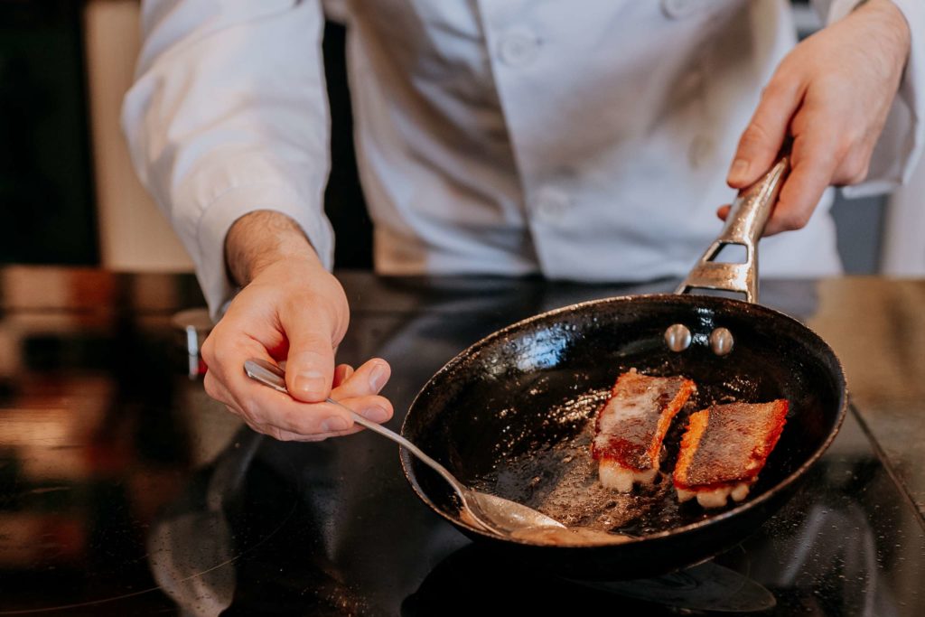 A chef cooking with a pan during a fine-dining experience at Swinton Cookery School