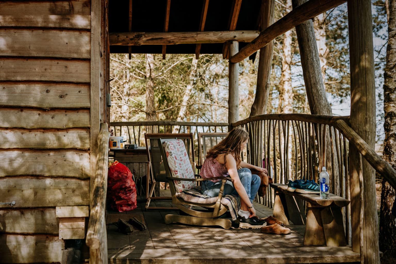 A woman sitting on the porch of an outdoor woodland lodge at Swinton Bivouac in Yorkshire