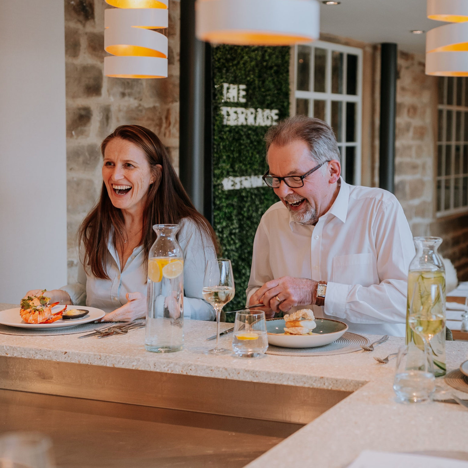 A laughing man and woman eating a meal in The Terrace Restaurant and Bar at Swinton Estate