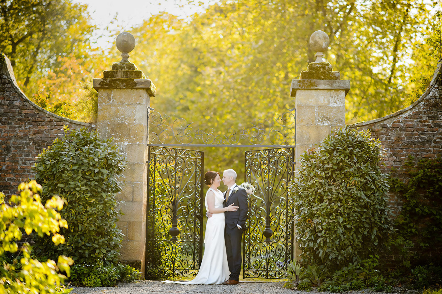 Happy newlyweds standing in front of the gate in the walled garden at Swinton Park in North Yorkshire. Photo by Ryan Browne.