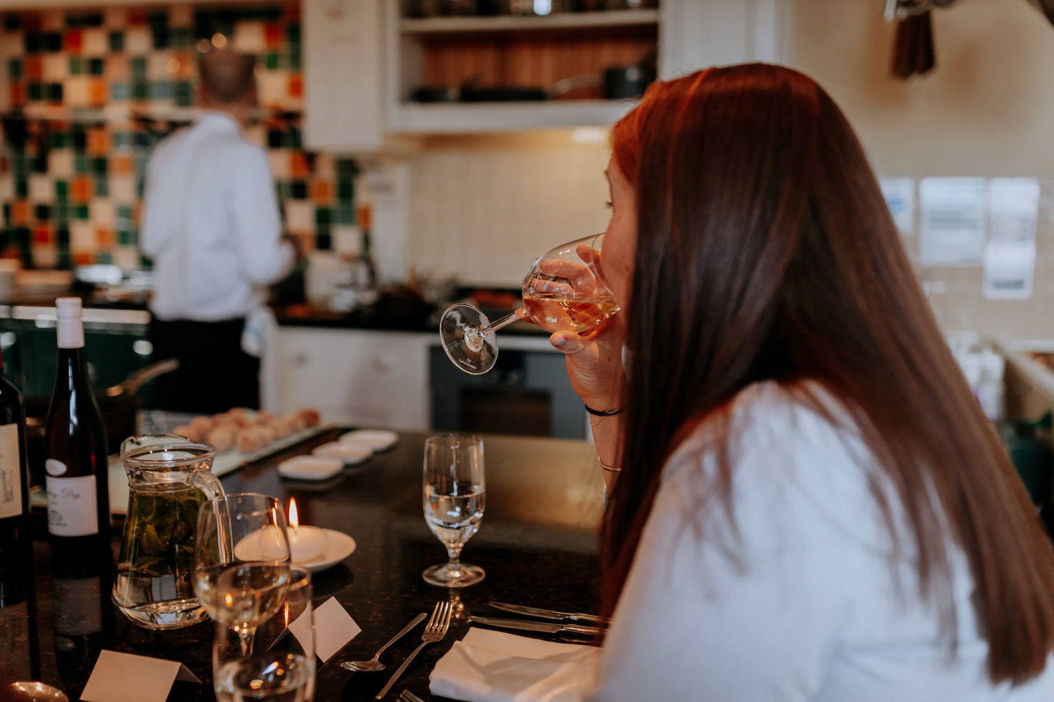 A woman drinking from a glass of wine during a Chef's Table experience at Swinton cookery School