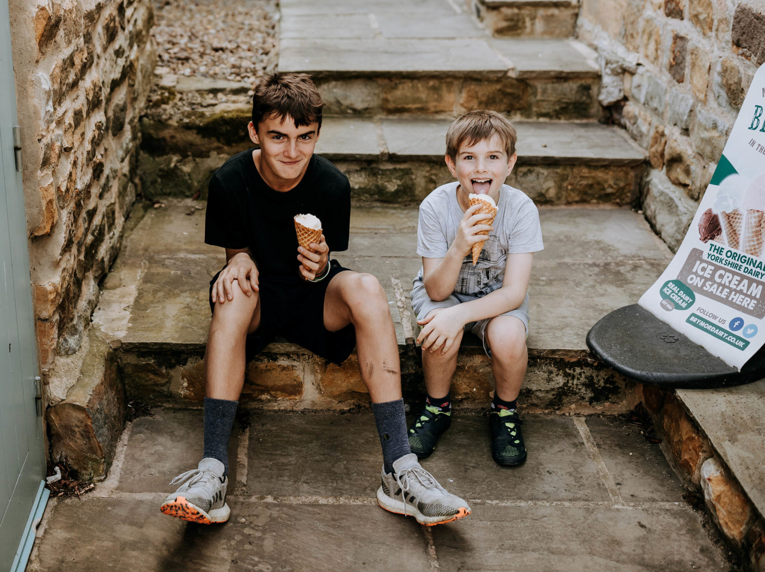 Two children eating ice cream as they sit on a stone step at Swinton Bivouac in North Yorkshire