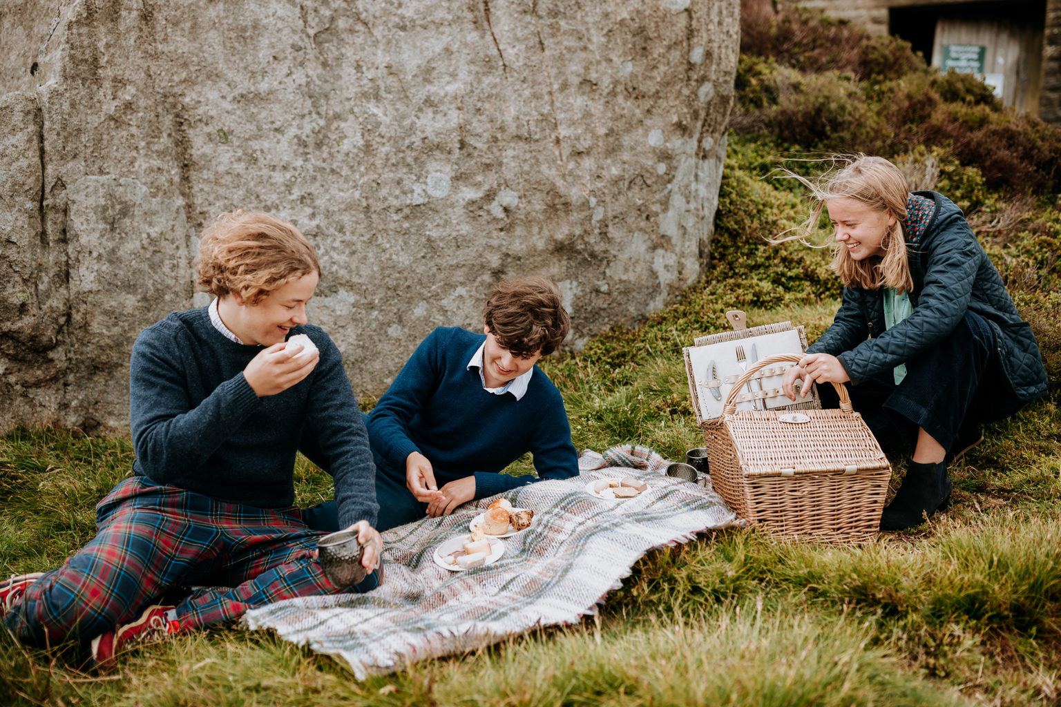 Three teenagers having a picnic outdoors on grass on the Swinton Estate in North Yorkshire.