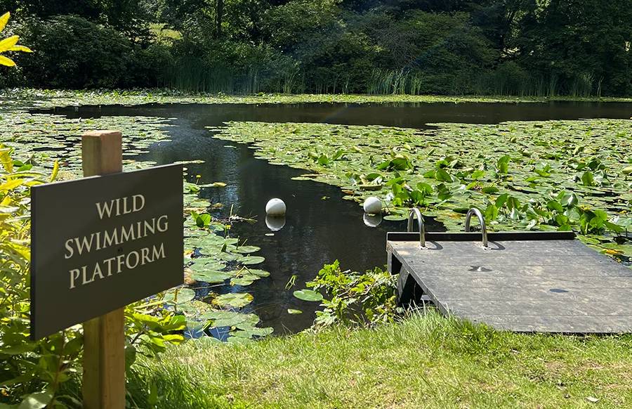 A sign saying "wild swimming" next to a lake at Swinton Estate