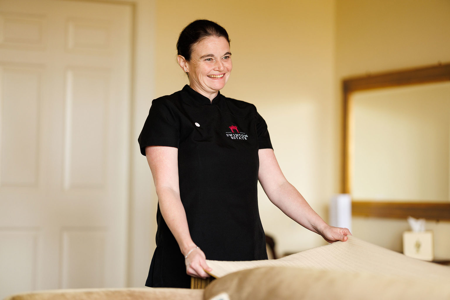 A smiling hospitality employee making a bed at Swinton Park Hotel