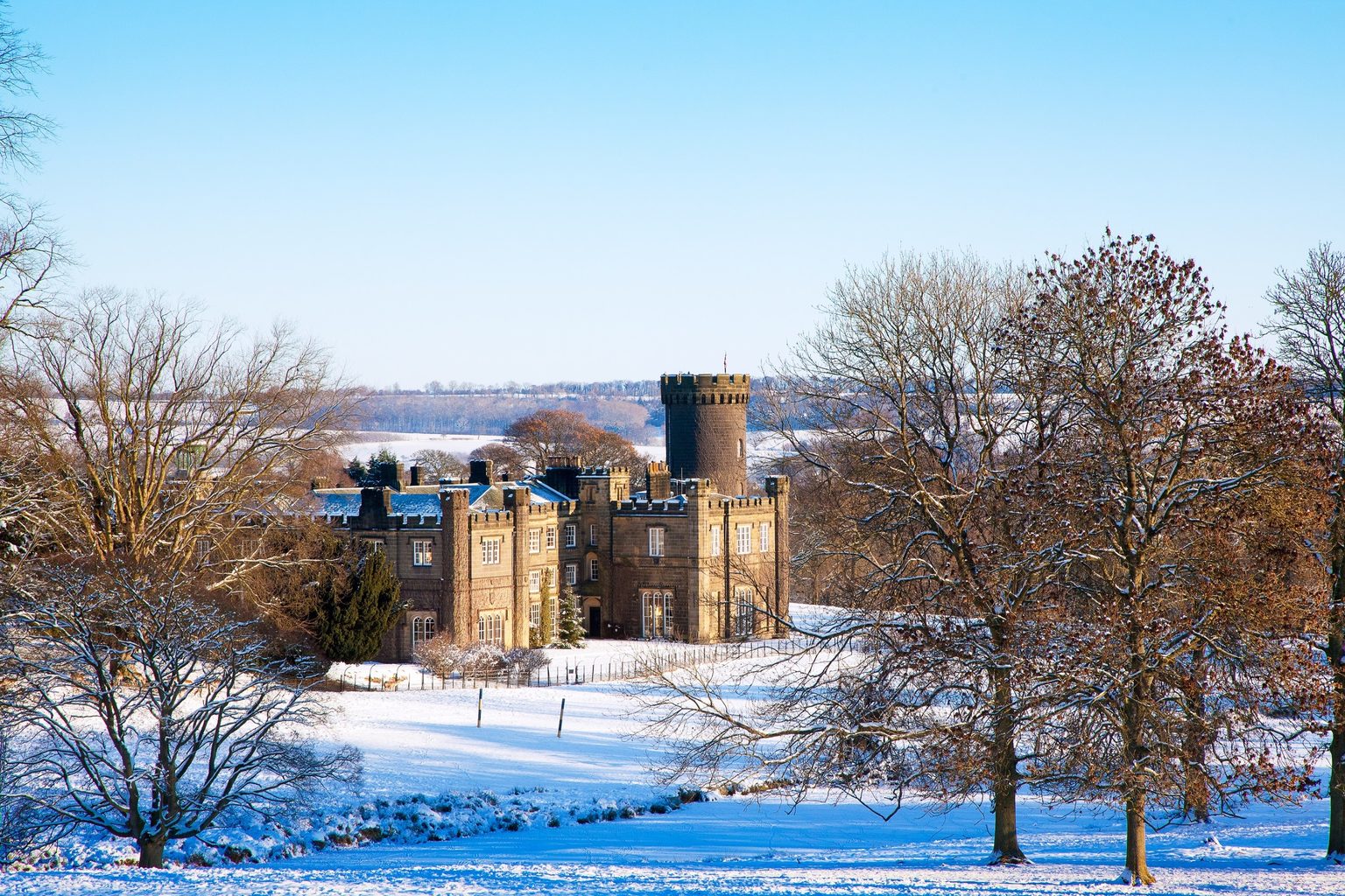 The castle-like exterior of Swinton Park Hotel surrounded by winter snow during at Christmas on the Swinton Estate Harrogate and the North Yorkshire Dales.