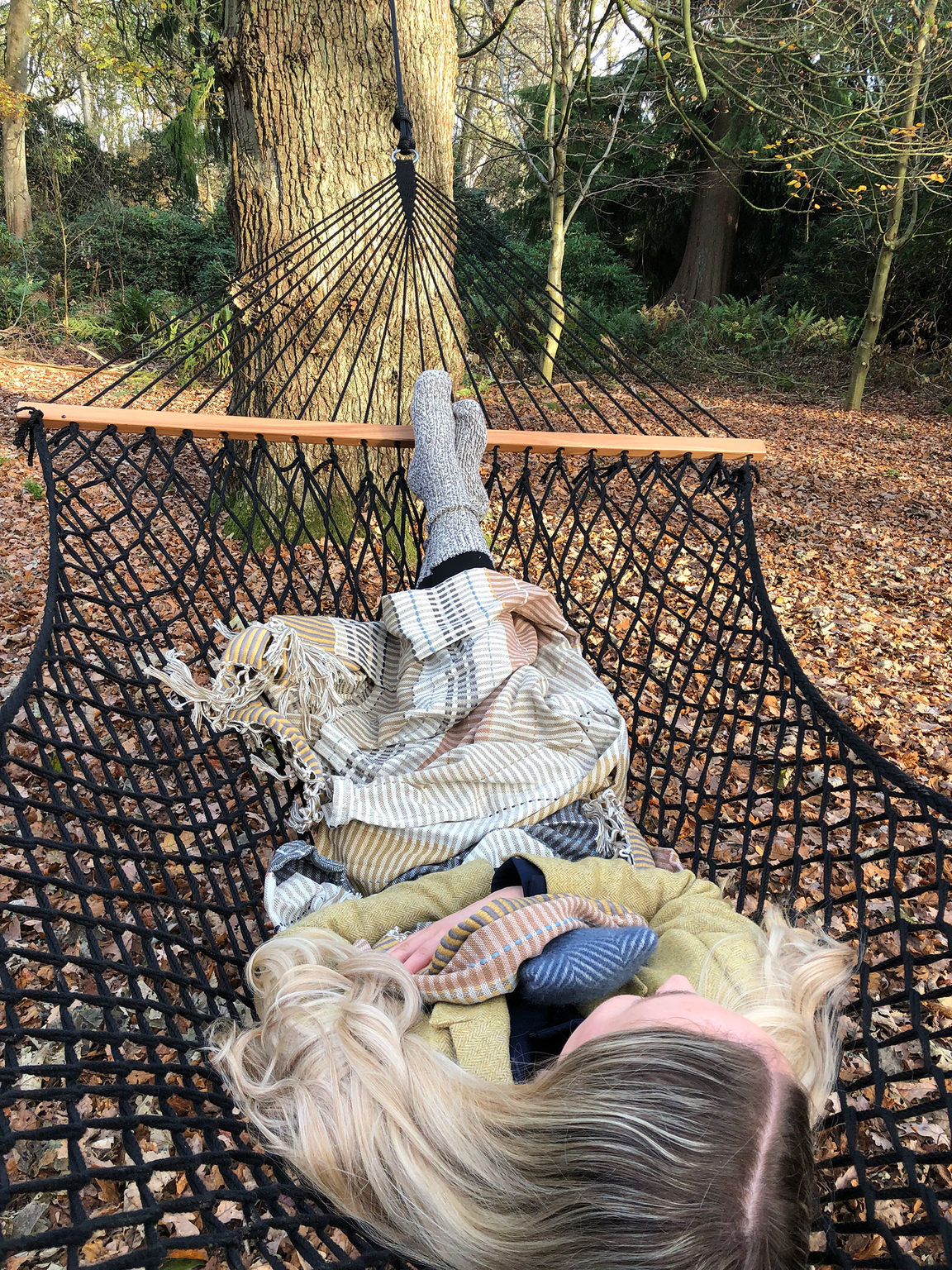 A woman lying in a woodland hammock in the outdoor wellbeing space at Swinton Country Club and Spa in North Yorkshire.