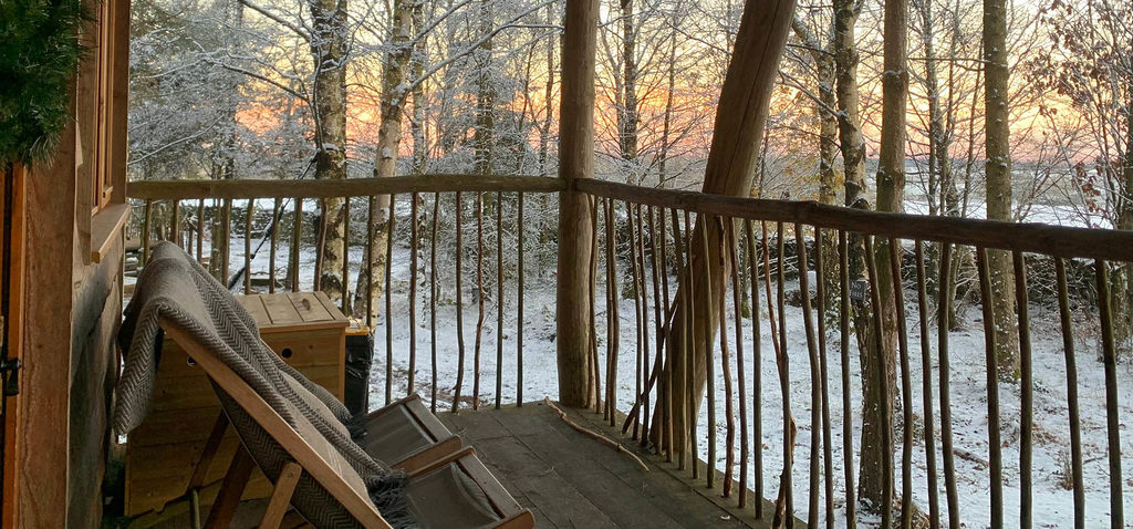 A wooden chair on the veranda of a luxury holiday Tree Lodge looking out at a snowy Christmas landscape in North Yorkshire